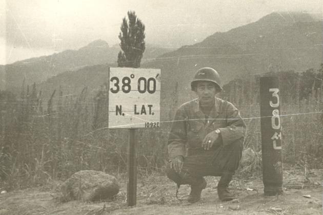 Black and white photo Kay K. Sasaki in US military uniform posing next to 38' 00" N. Lat. sign