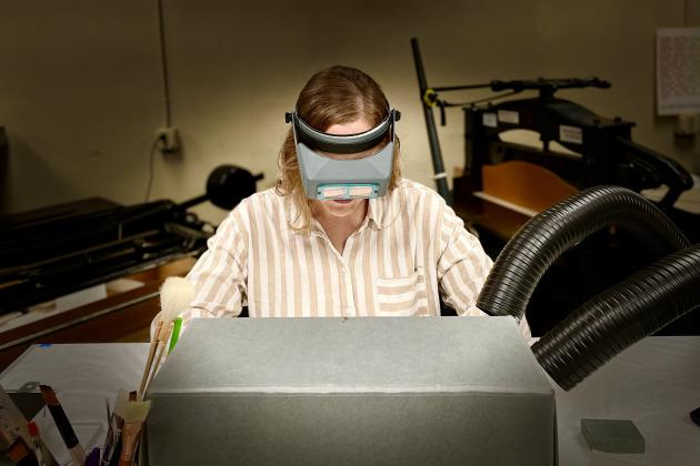 Photograph of person doing conservation work partially hidden by an archival box