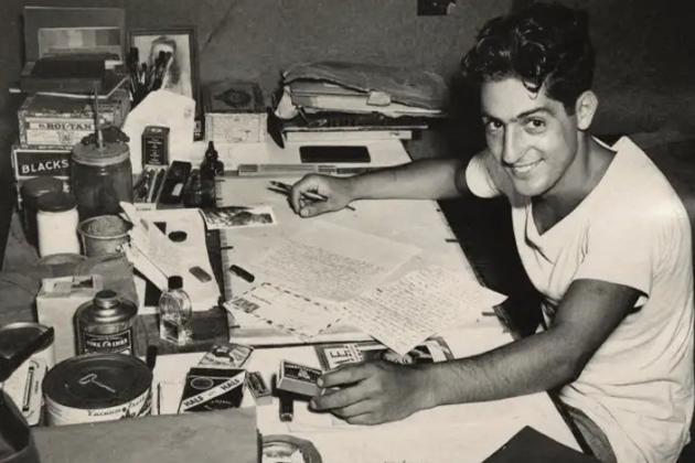 Nat Bellantoni writting a letter at his desk in a tent during World War II