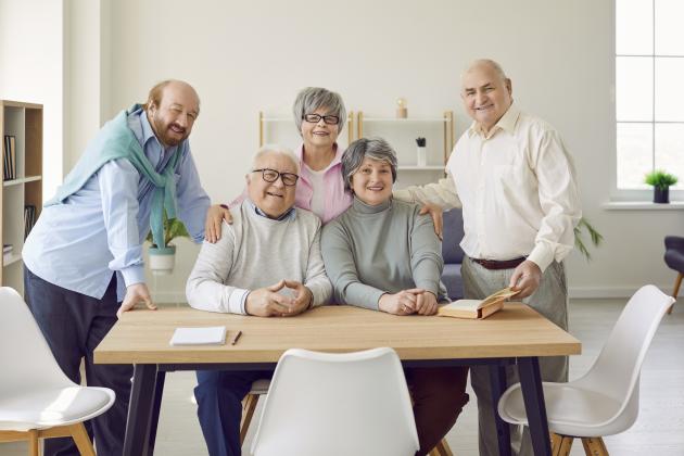 Group of senior people men and women sitting in nursing home at the table and looking at camera. - stock photo