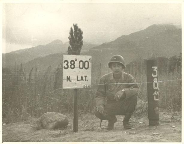 Black and white photo Kay K. Sasaki in US military uniform posing next to 38' 00" N. Lat. sign