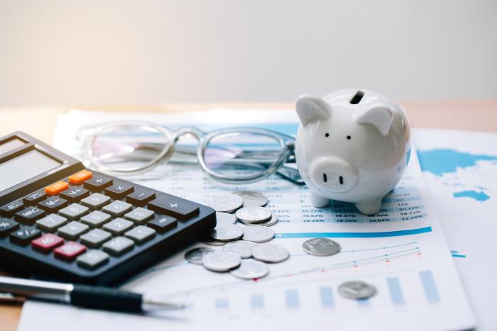 Piggy bank, coins, glasses, and calculator on top of paper