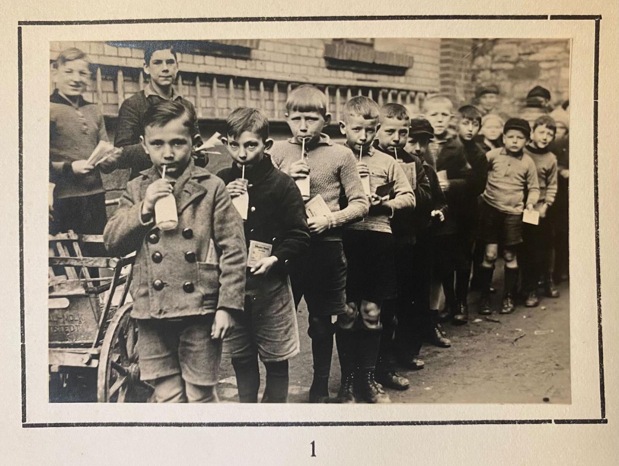 Group of children standing in line drinking from a bottle with a straw