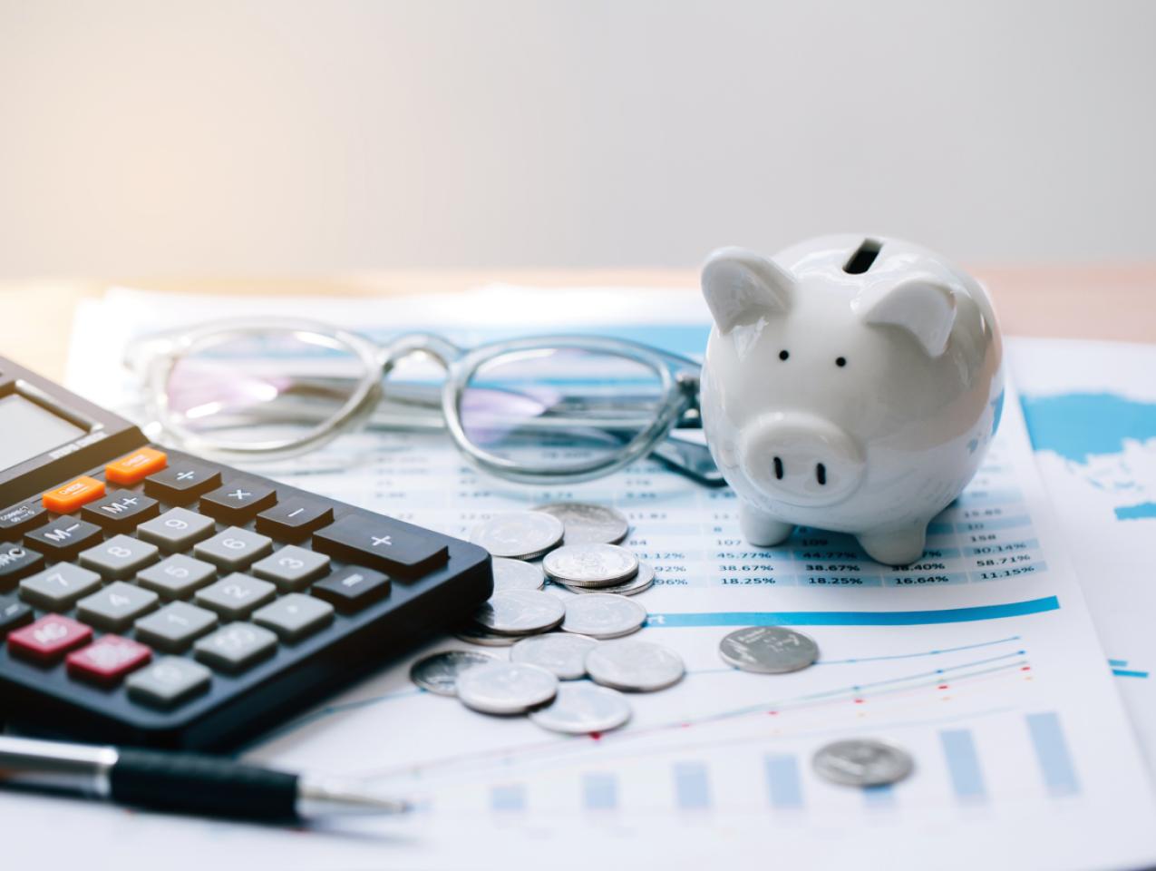 Piggy bank, coins, glasses, and calculator on top of paper
