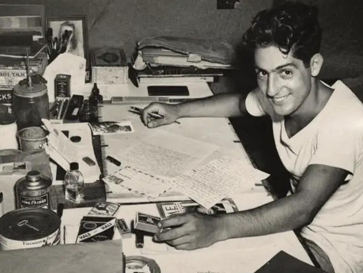 Nat Bellantoni writting a letter at his desk in a tent during World War II
