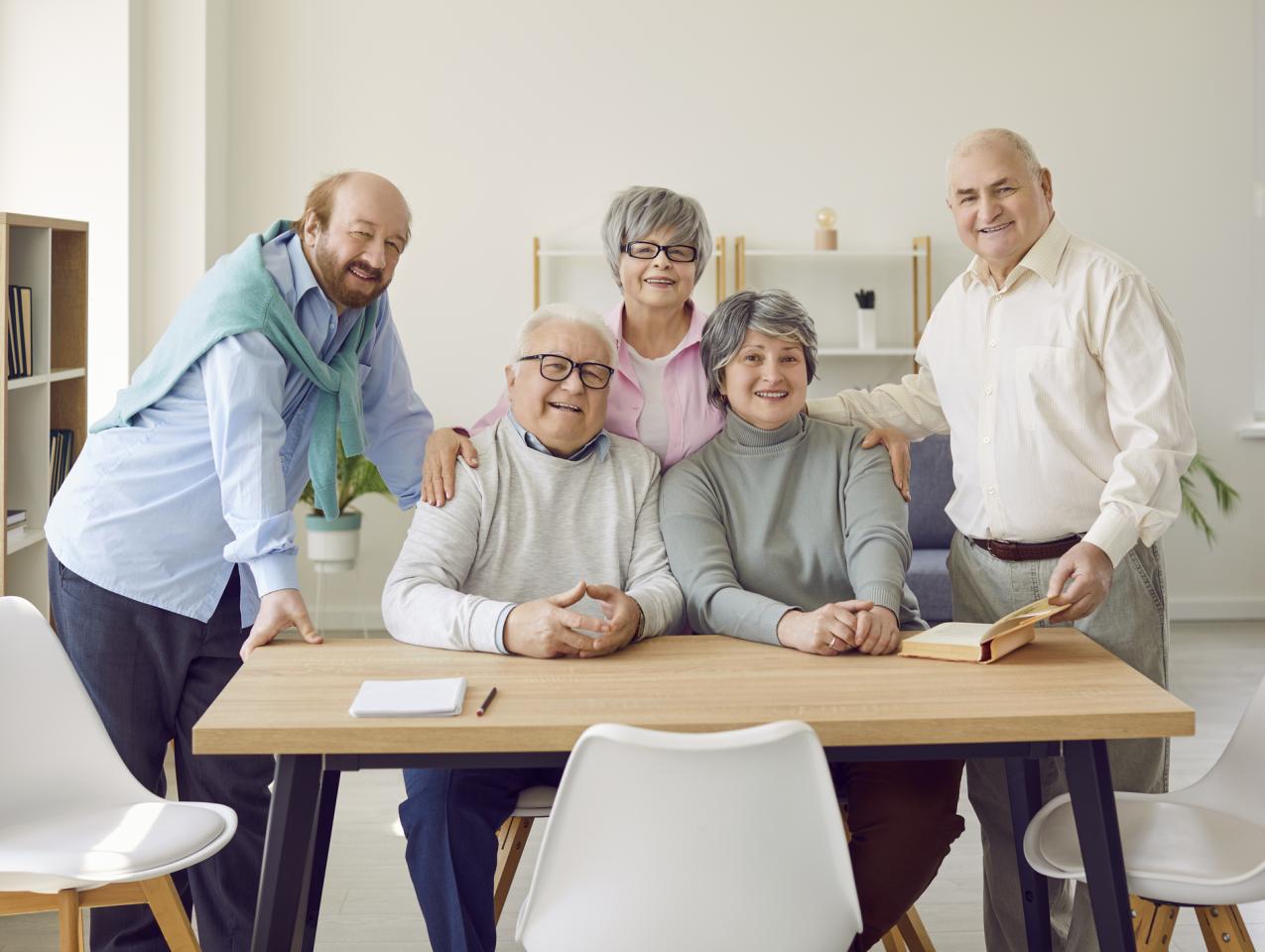 Group of senior people men and women sitting in nursing home at the table and looking at camera. - stock photo