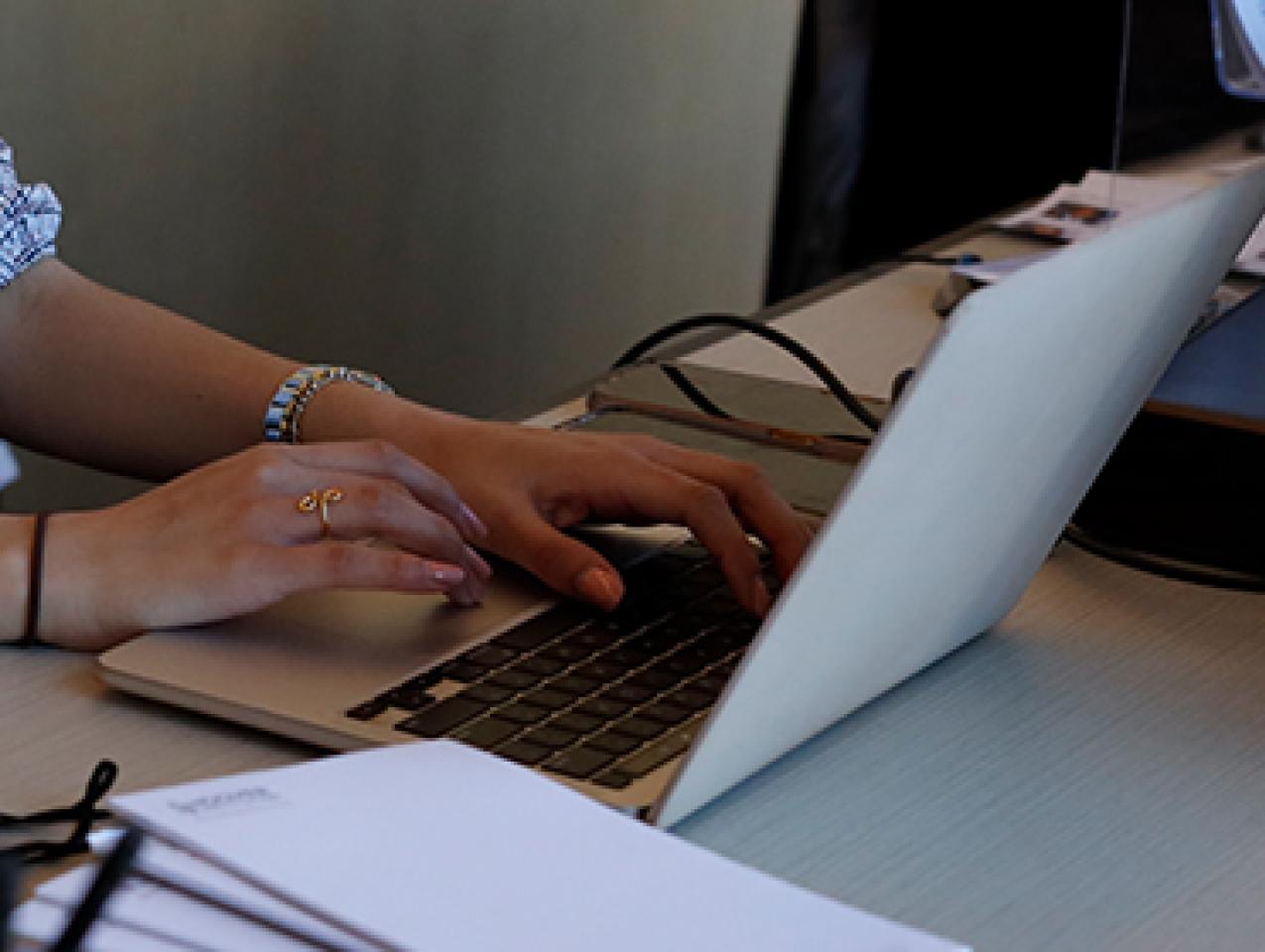 color photograph of a woman's hands typing on a laptop computer