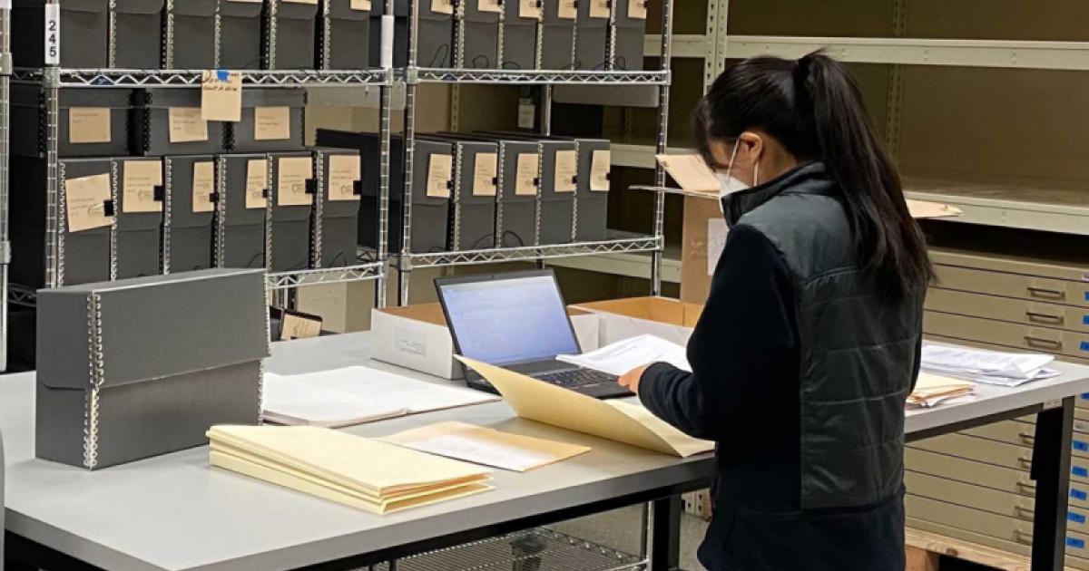 Jessica Y standing in front of a table with documents, laptop, and manuscript boxes