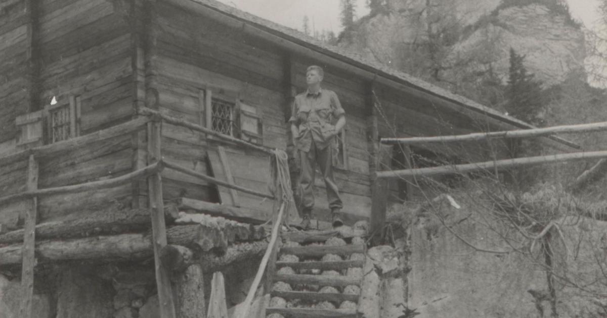 US soldier Donald Wayne Richardson standing in front of a log cabin.