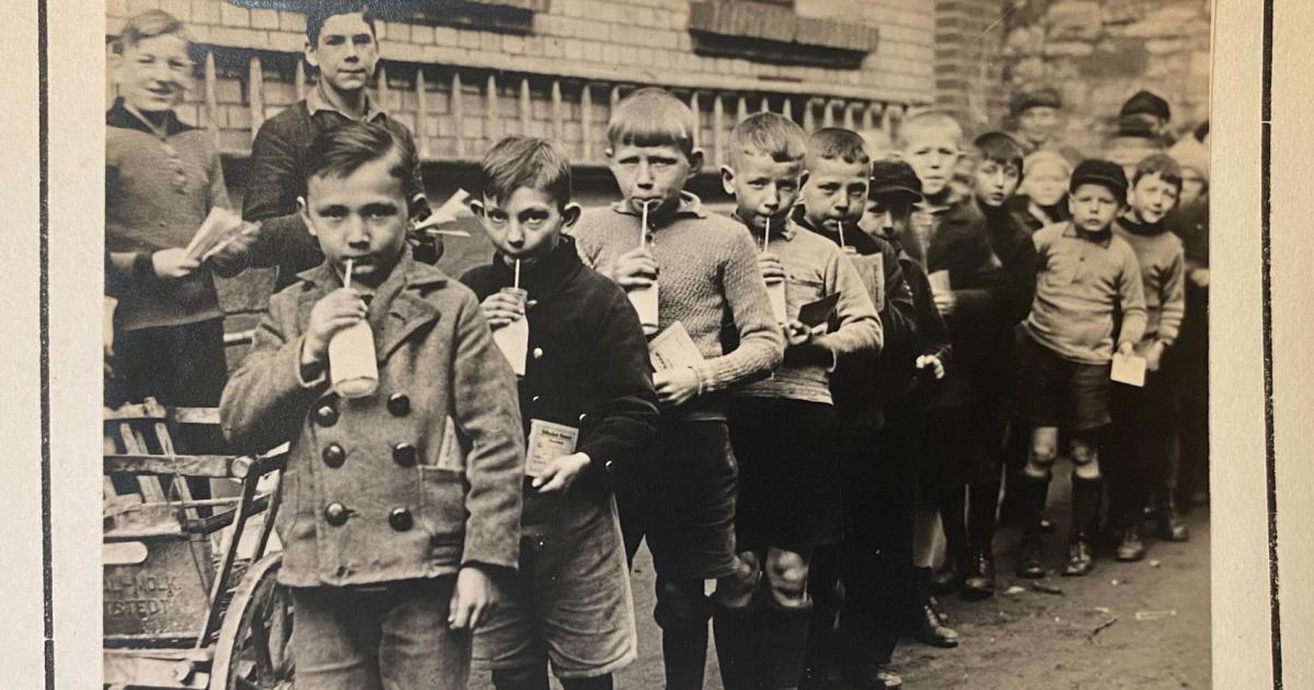 Group of children standing in line drinking from a bottle with a straw