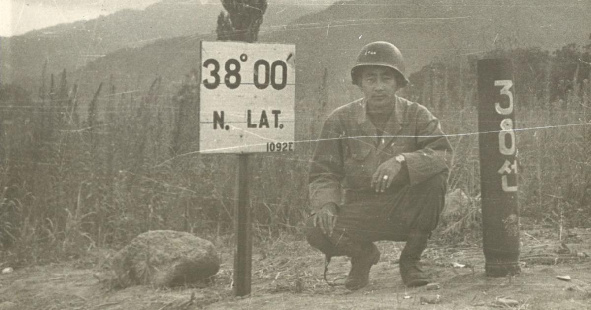 Black and white photo Kay K. Sasaki in US military uniform posing next to 38' 00" N. Lat. sign