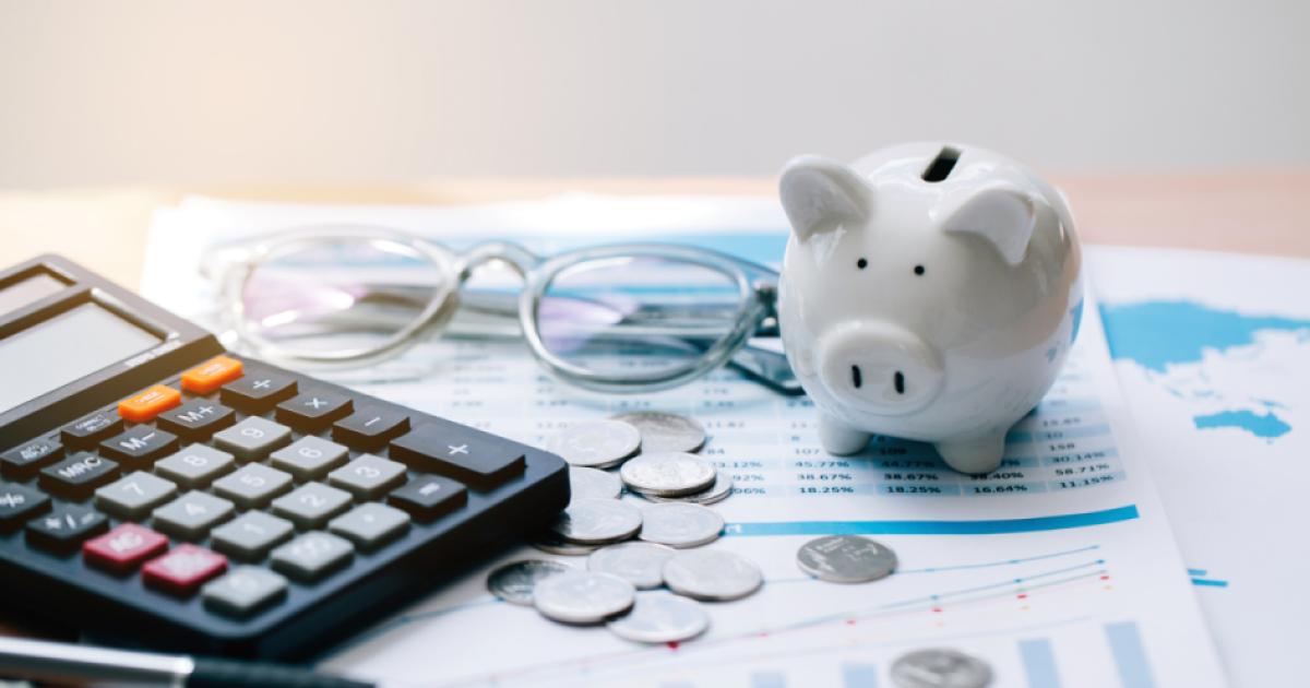 Piggy bank, coins, glasses, and calculator on top of paper