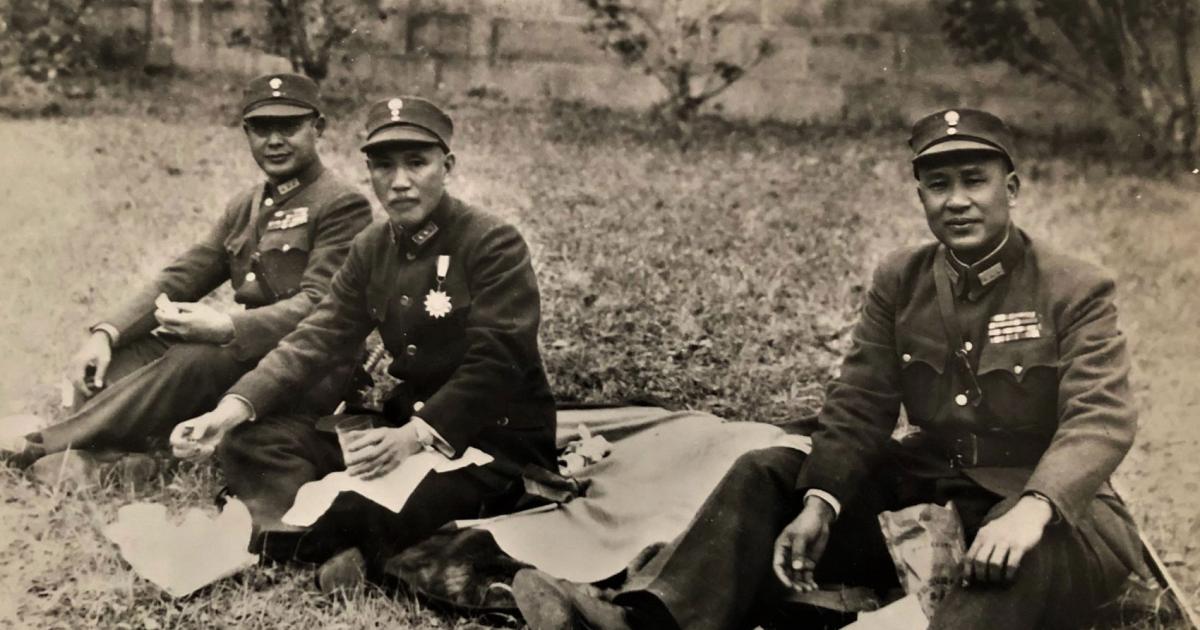 Black and white photo of 3 men dressed in military uniforms sitting on the ground having a picnic.