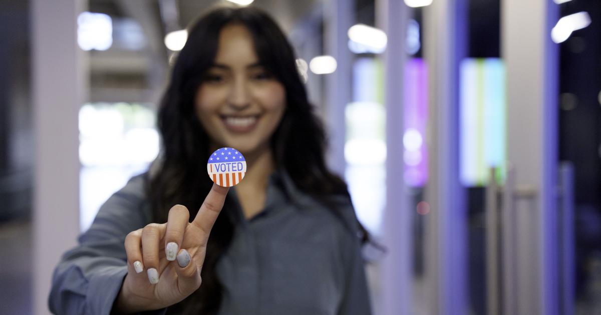 Young Hispanic Woman in Her Twenties Proudly Displaying Her I Voted Sticker in a Co-Working Space stock photo