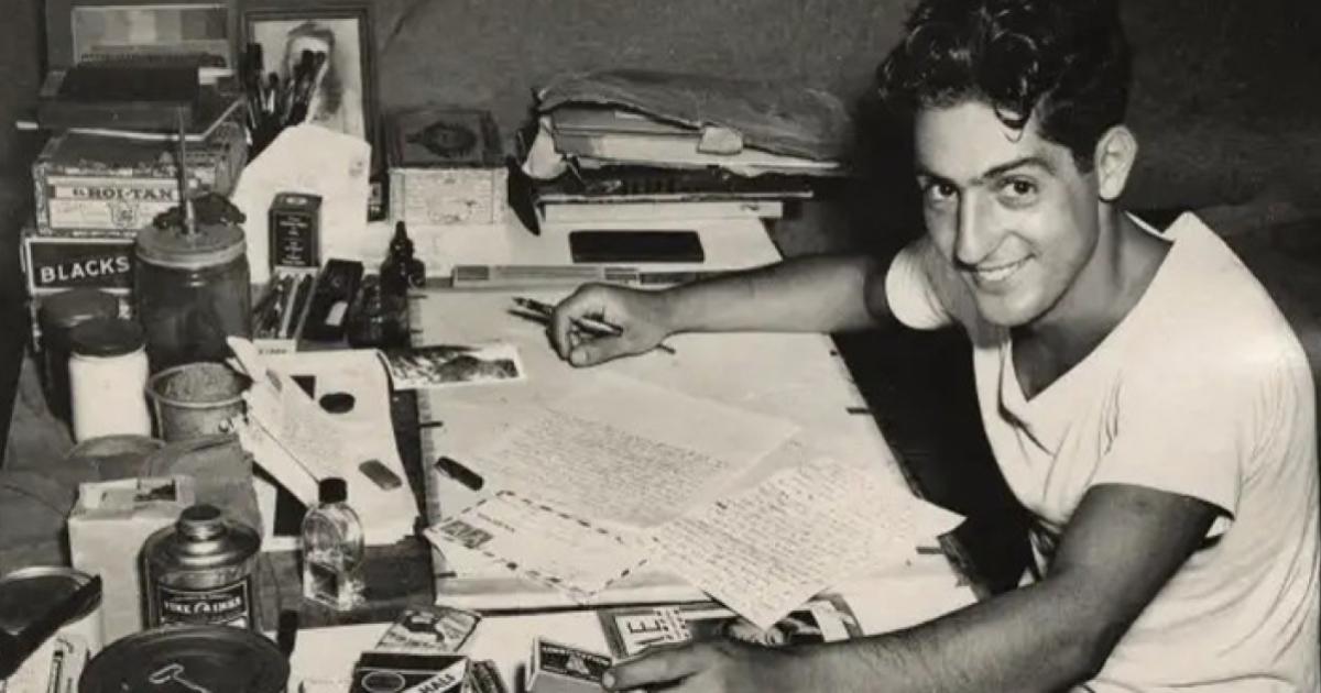 Nat Bellantoni writting a letter at his desk in a tent during World War II