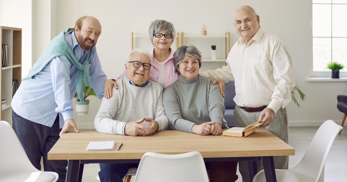 Group of senior people men and women sitting in nursing home at the table and looking at camera. - stock photo