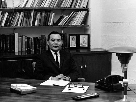 Black and white photo of Eugene Wu sitting at a desk with a bookshelf in the background