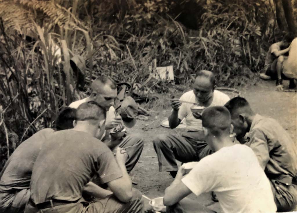 Black and white photo of a group of men sitting on the ground eating